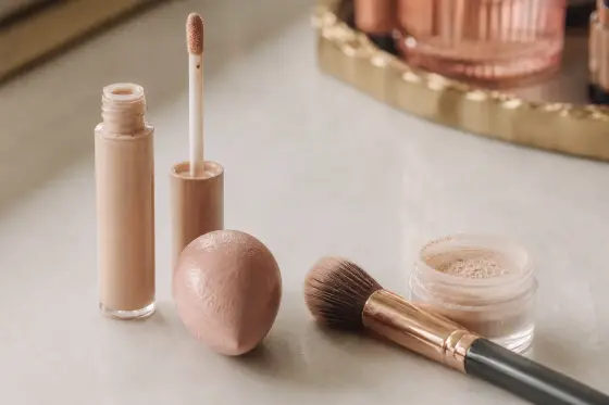 Pinceau estompeur, éponge rosée et tube de correcteur sans étiquette sur une coiffeuse claire