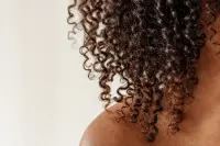 Mèches de cheveux bouclés texturés captant la lumière naturelle, fond neutre