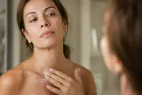Femme appliquant une crème du bout des doigts sur son cou et son décolleté devant un miroir