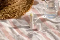 Stick à lèvres solaire sans étiquette et chapeau de paille posés sur une serviette de plage