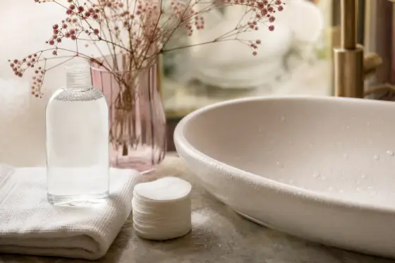 Flacon d’eau micellaire sans étiquette, disques de coton et serviette blanche près d’un lavabo