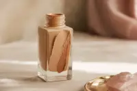 Flacon de fond de teint renversé sur une surface claire, traînée de produit, lumière douce