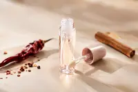 Tube de gloss transparent ouvert, piment séché et bâton de cannelle sur une surface claire