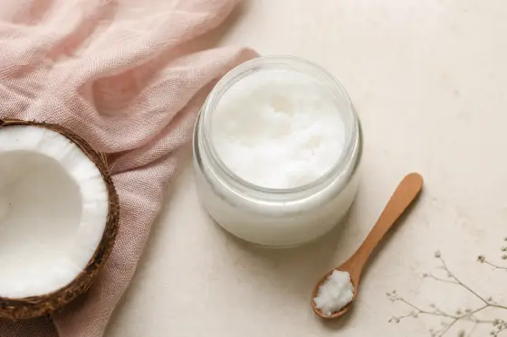 Pot ouvert d’huile de coco blanche et solide, cuillère en bois et noix de coco sur un plan clair