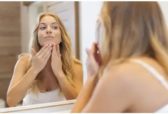 Flacon d’exfoliant liquide, coton réutilisable et serviette blanche posés près d’un miroir