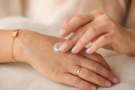 Gros plan sur des mains d’adulte appliquant une crème hydratante, lumière naturelle douce