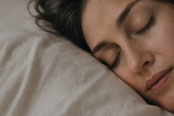 Visage au repos sur un oreiller clair, lumière tamisée du petit matin, peau nette sans maquillage