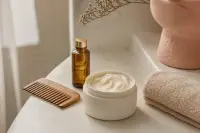 Pot de masque capillaire ouvert, peigne à dents larges et serviette éponge sur un plan clair