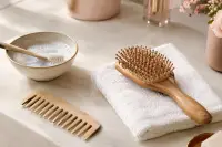 Brosse à cheveux en bois et peigne posés près d’un bol d’eau savonneuse sur un plan clair
