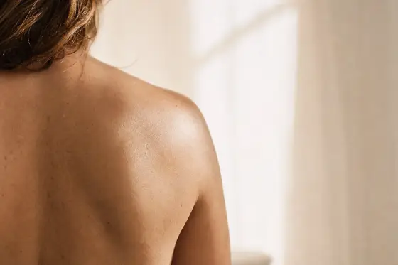 Peau nue du haut du dos et de l’épaule, texture naturelle, lumière douce du matin