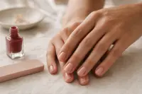 Mains aux ongles courts et naturels posées près d’un flacon de vernis rouge sans étiquette