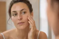 Femme d’une trentaine d’années appliquant un sérum du bout des doigts devant un miroir de salle de bain