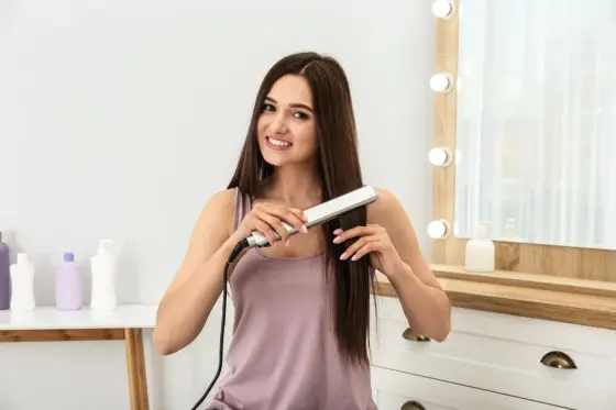 Fer à lisser ouvert près de mèches de cheveux bruns secs et démêlés sur une coiffeuse
