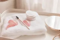 Brosse à cils propre, petit miroir et coton posés sur une tablette de soin claire