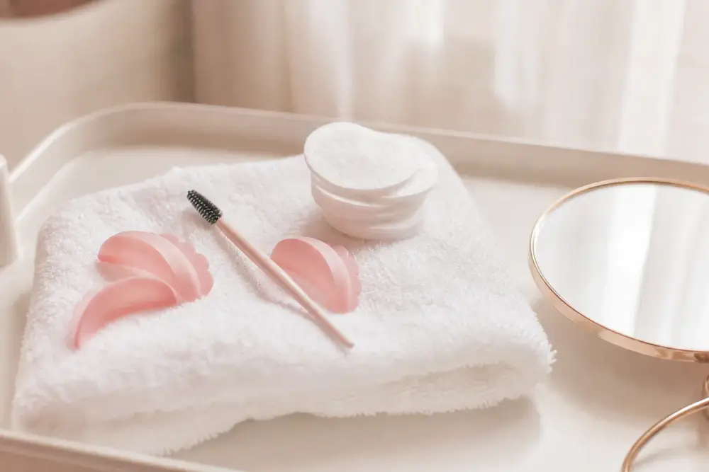 Brosse à cils propre, petit miroir et coton posés sur une tablette de soin claire