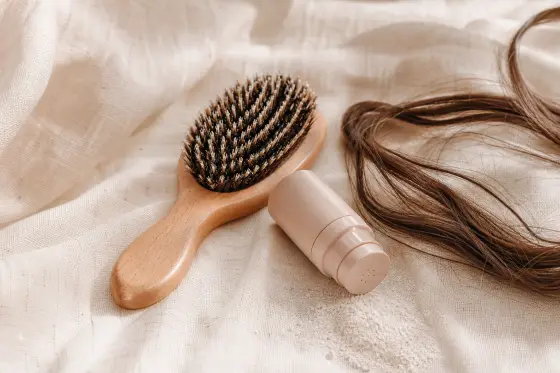 Brosse en bois et petit flacon poudreur sans étiquette posés près de longues mèches brunes