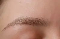 Sourcil naturel épars photographié de près, quelques poils fins et espacés sur peau claire
