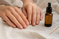Mains aux ongles courts et nus posées sur un linge clair près d’un flacon d’huile