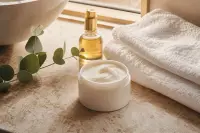Pot de crème corps ouvert et serviette en coton sur un plan de salle de bains baigné de lumière