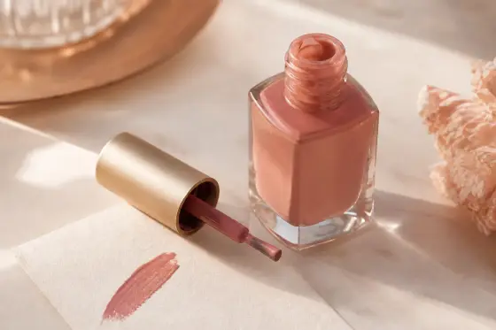 Flacon de vernis à ongles ouvert sur une surface claire, pinceau posé à côté, lumière douce
